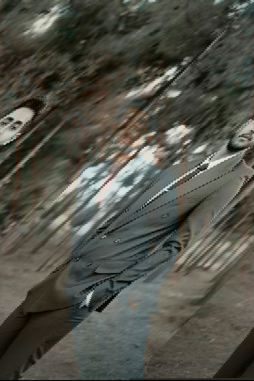 a man in a suit standing in a forest